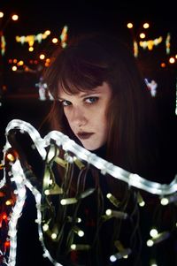 Portrait of young woman standing by illuminated decorations at night