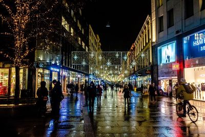 People in illuminated city against sky at night