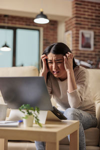 Worried woman with head in hands looking at laptop