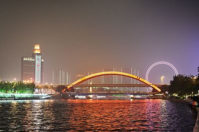 Illuminated bridge over river in city against clear sky at night
