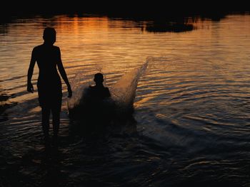 Silhouette boys enjoying in lake during sunset