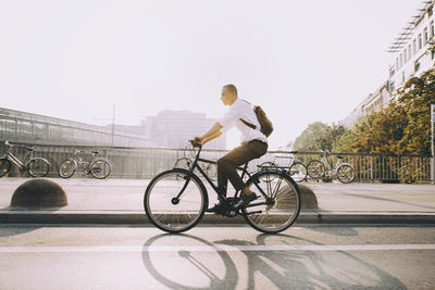 Full length of businessman riding bicycle on street in city against sky