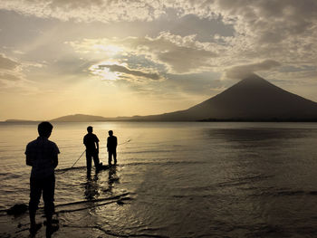 Silhouette people on shore against sky during sunset