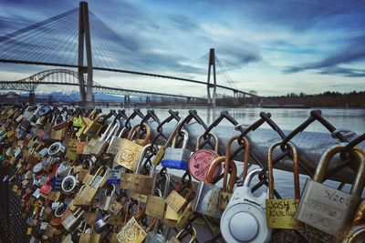 Love padlocks tied up on fence by skybridge over fraser river against sky