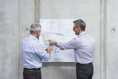 Two businessmen discussing construction plan at concrete wall