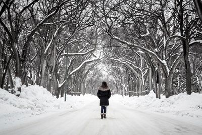 Rear view of woman walking on snow covered road