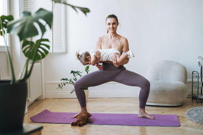 Young woman fit mom with baby girl in her arms doing fitness on mat at home