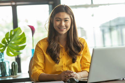 Portrait of smiling businesswoman with laptop on desk sitting in office