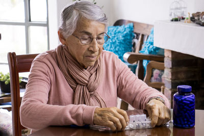 Senior woman taking medicine while sitting by table at home