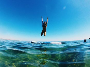 Woman jumping in sea against clear blue sky