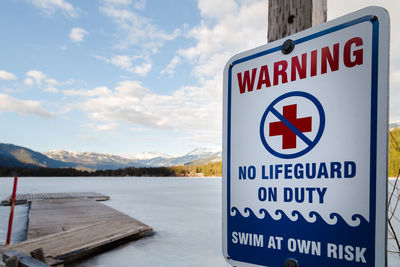 Warning sign by lake against sky