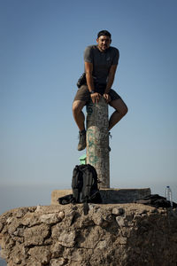 Low angle view of man standing on rock against clear sky