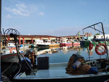 People sitting on boats moored at harbor against sky