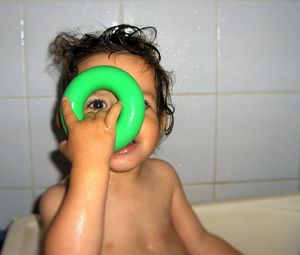 Portrait of baby looking through toy ring while bathing