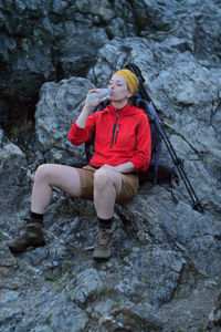Full length of woman drinking water while sitting on rock formation