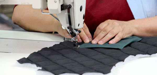 Midsection of tailor using sewing machine while stitching textile