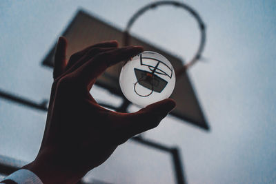 Close-up of hand holding crystal ball against basketball hoop