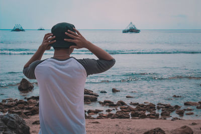 Rear view of man standing at beach against sky