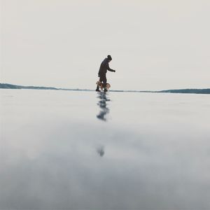 Side view of woman with dog standing at beach against sky