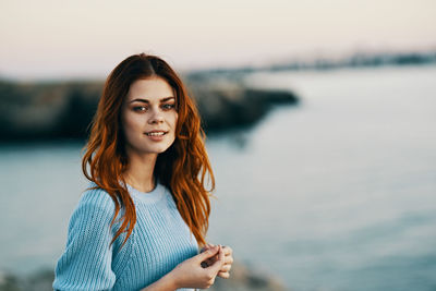 Portrait of smiling young woman standing against sea