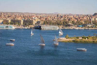 Sailboats sailing on sea by city against sky