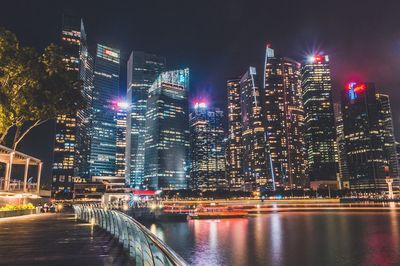 Illuminated buildings by river against sky at night