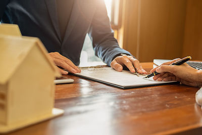 Close-up of estate agent and client signing contract on table