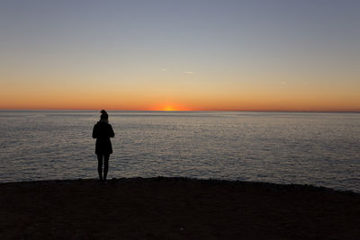 Silhouette man standing on beach against sky during sunset