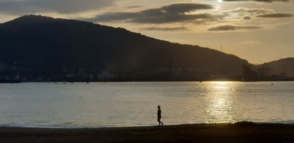 Silhouette man standing on beach against sky during sunset