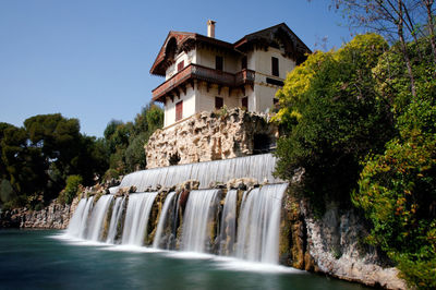 Waterfall amidst trees and buildings against clear sky