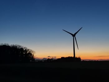 Silhouette wind turbines on field against sky during sunset