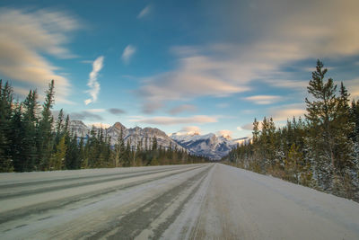 Empty road by snowcapped mountains against sky