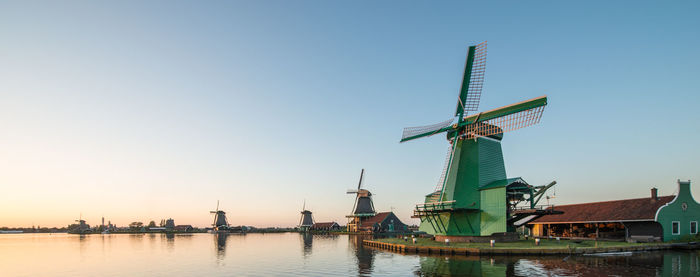 Panoramic of traditional windmills by canal at zaanse schans against clear sky