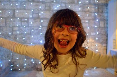 Close-up of happy girl against illuminated lights on wall