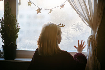 Rear view of girl drawing snowflakes on window