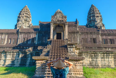 Rear view of woman wearing asian style conical hat standing by temple