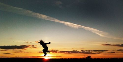 Silhouette of woman jumping in sky at sunset