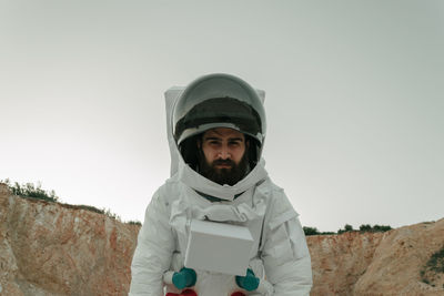 Low angle portrait of male astronaut standing on field against sky