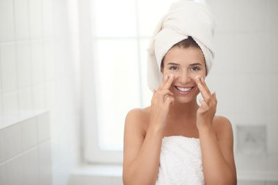 Portrait of smiling young woman applying moisturizer on face in bathroom