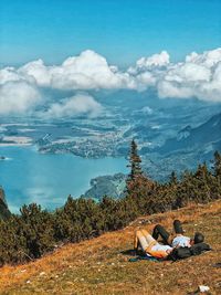 High angle view of couple lying on mountain against cloudy sky