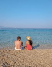 Rear view of woman sitting at beach against clear blue sky