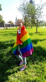 Cheerful teenage girl with rainbow flag standing on field