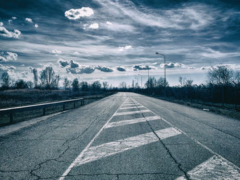 Empty road by trees against sky