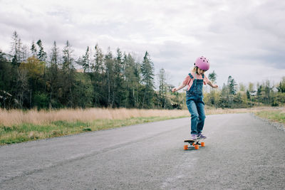 Young girl learning to skateboard on a country road