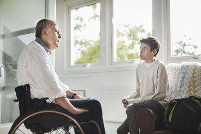 Disabled father in wheelchair talking to son at home