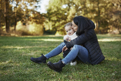 Mother and daughter sitting and hugging in autumn park