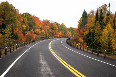 Road by trees against sky during autumn