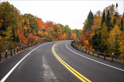 Road by trees against sky during autumn