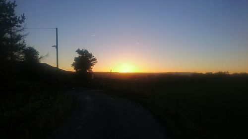 Road amidst silhouette trees against clear sky during sunset