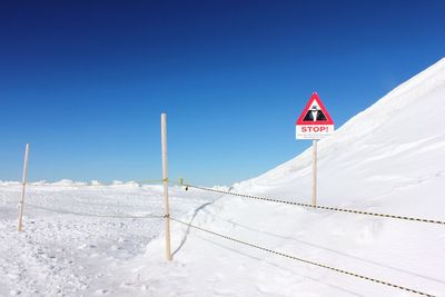 Road sign on snow covered landscape against clear blue sky